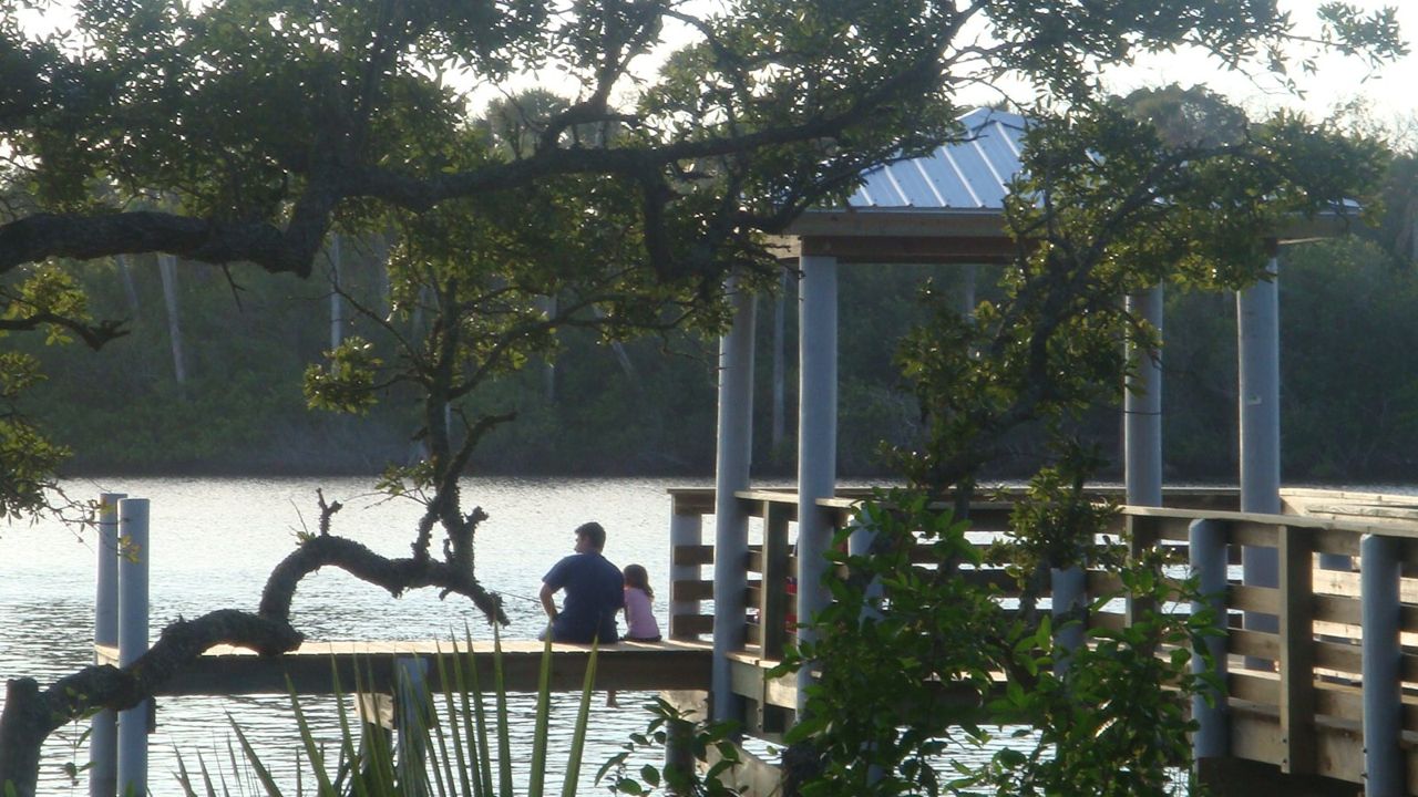 A father and his daughter sit at the dock of Seabridge Park, enjoying the calm waters and beautiful scenery.